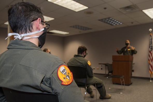 service members listen to a briefing wearing cloth masks and social distancing.