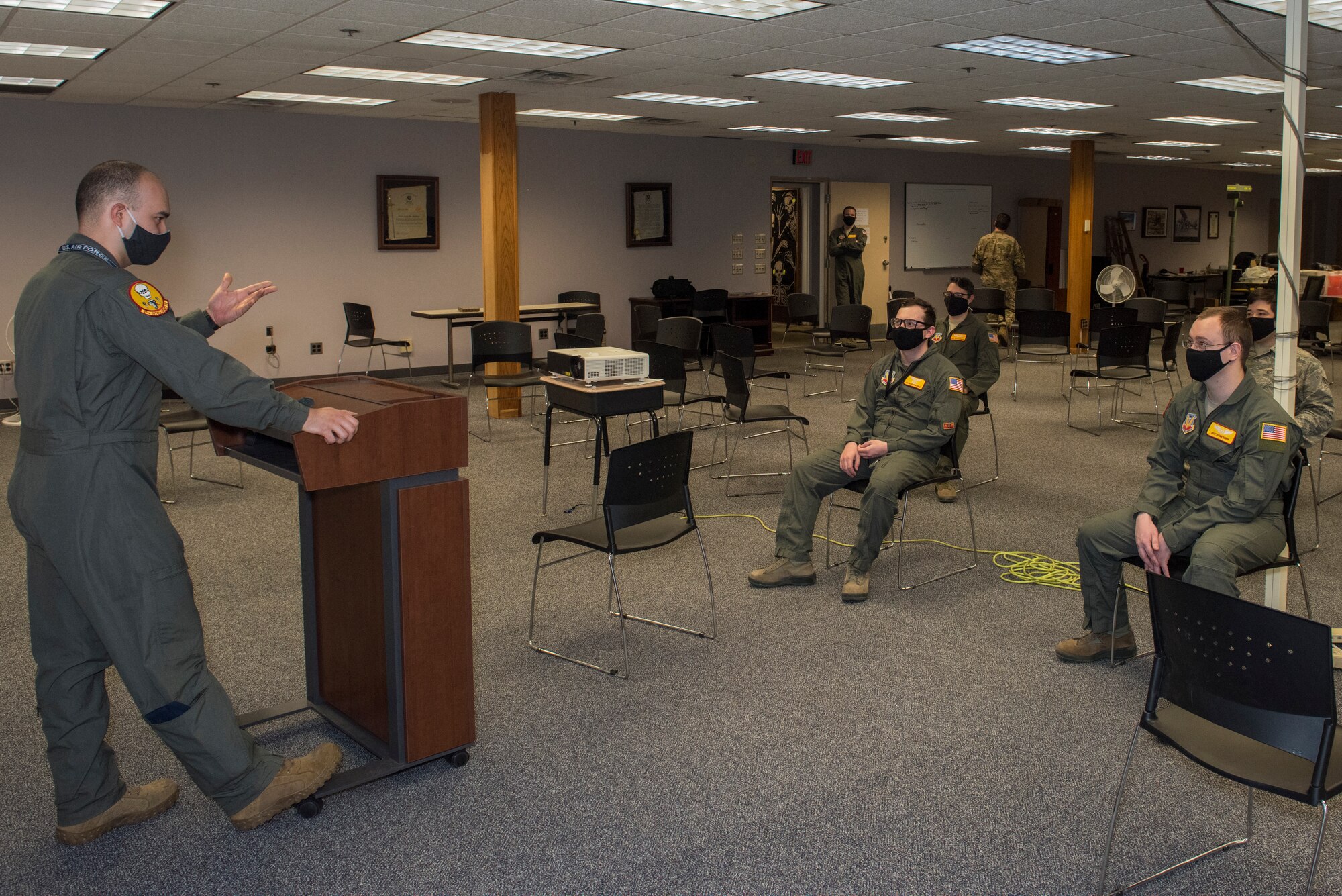 A service member briefs four service members while the group practices social distancing and wears cloth masks