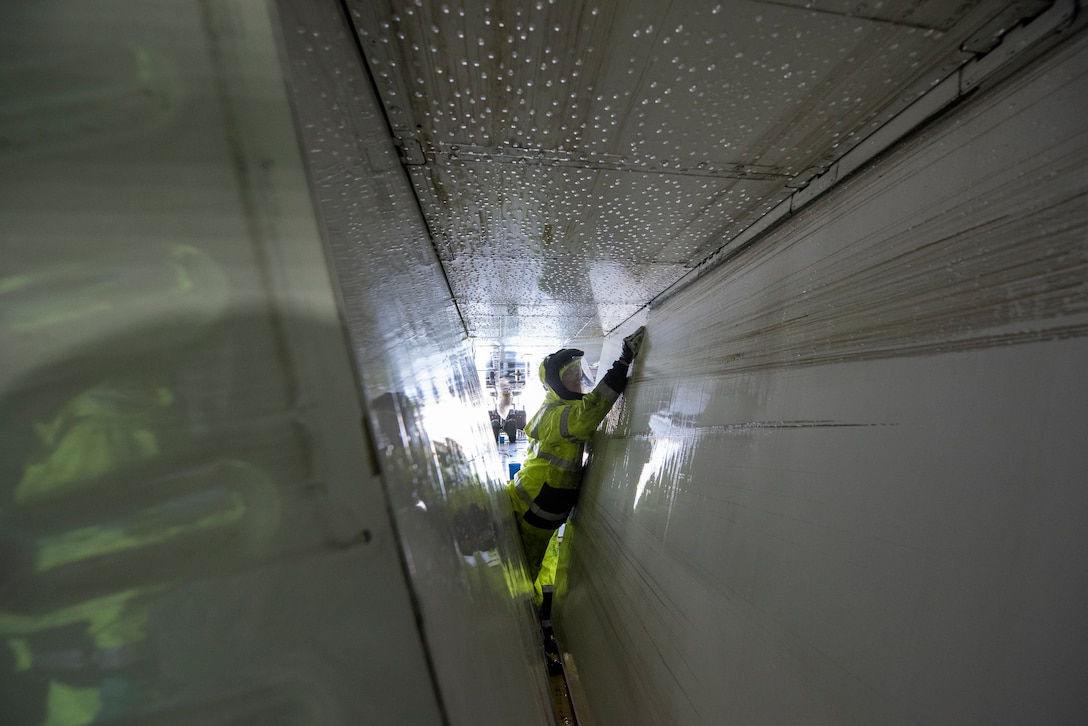 A man wearing protective equipment and gloves cleans the inside of an aircraft.