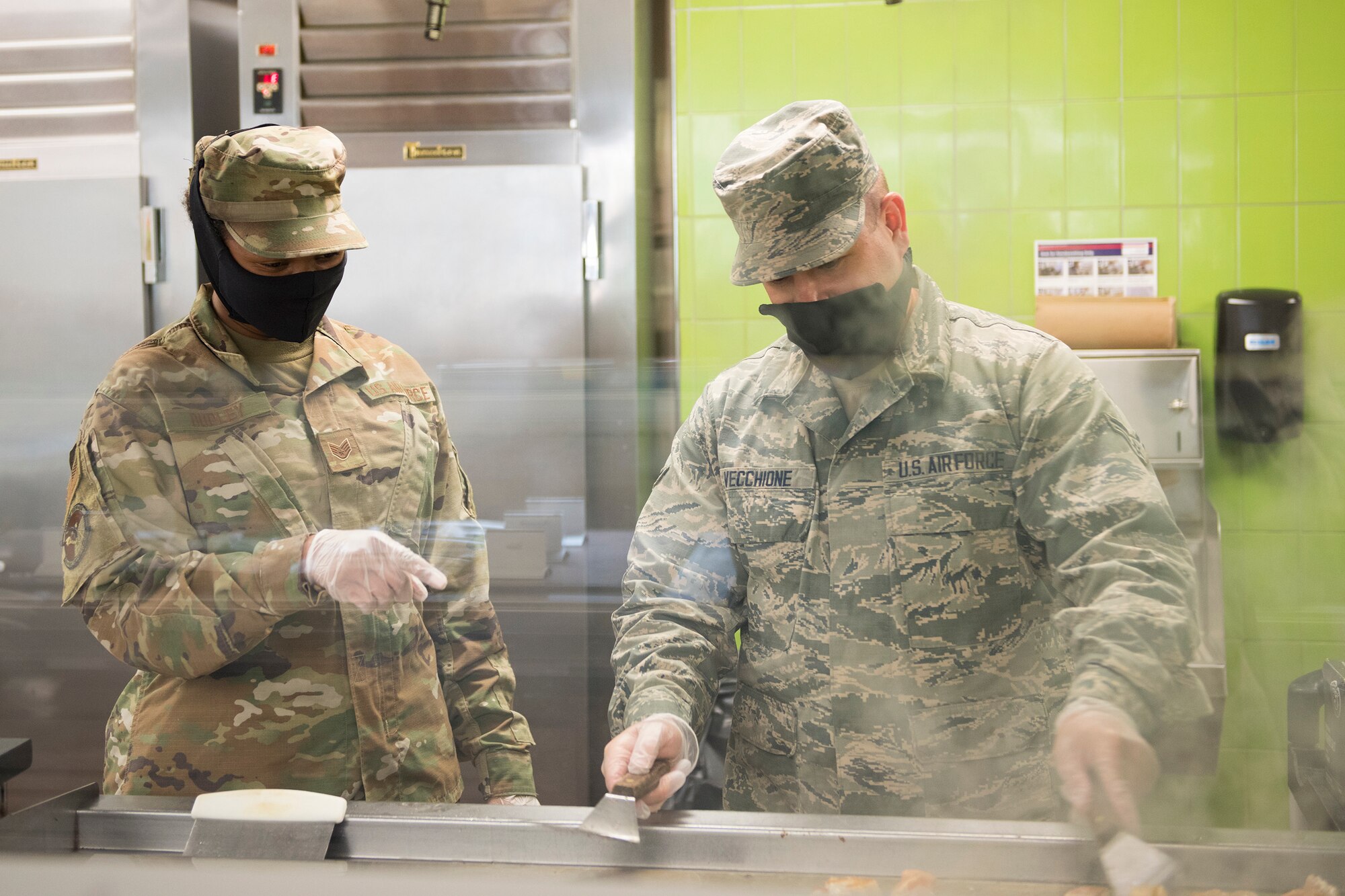 Staff Sgt. Shelona Dudley, (left) a food service journeyman assigned to the 628th Force Support Squadron supervises Airman 1st Class David Vecchione, also a food service journeyman assigned to the 628th Force Support Squadron, as he prepares food at the Gaylor Dining Facility at Joint Base Charleston, S.C., April 22, 2020. Dining facility personnel are cleaning more often, wearing masks and gloves and practicing physical distancing in order to protect themselves and customers. The DFAC is currently open for carry out only.