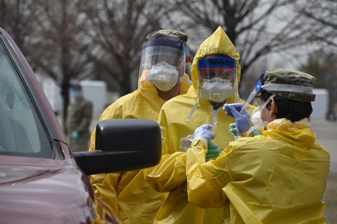 Photo of three 119th Medical Group Air National Guard members wearing personal protective equipment as they administer COVID-19 tests to volunteers from the community in the parking lot of the Alerus Center, Grand Forks, N.D., April 23, 2020.