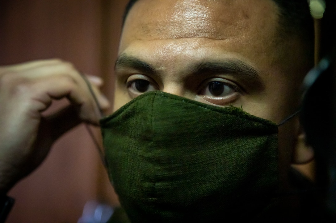 A Marine puts on a green cloth face mask to protect against the coronovirus