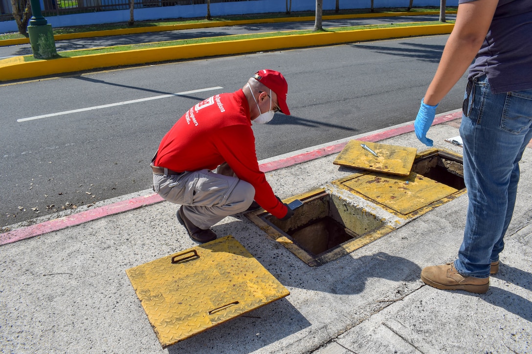 Ramon Collazos kneeling down on a sidewalk while examining the water supply .