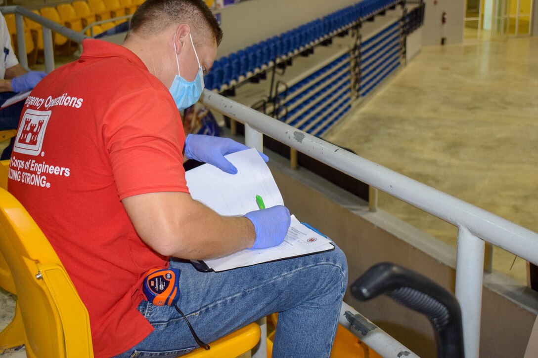 Edgardo Bermudez, wearing a mask and gloves, seating down and writing in a notebook.