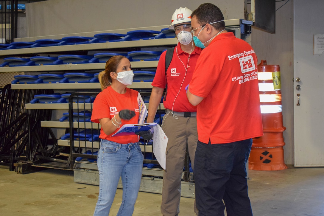 Maricarmen Crespo holds a clipboard while speaking to Hector Ortiz and Ivan Chong-Cruz. All three are standing up.