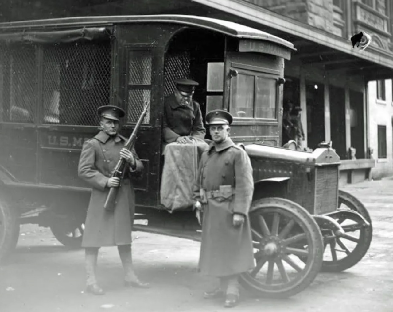Armed Marines stand beside mail delivery truck.