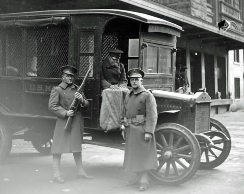 Armed Marines stand beside mail delivery truck.