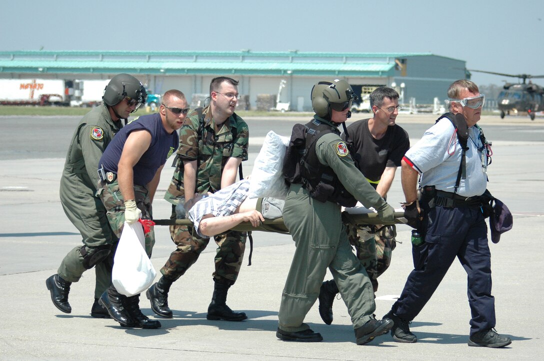 A patient on a stretcher is carried by military people across a tarmac.