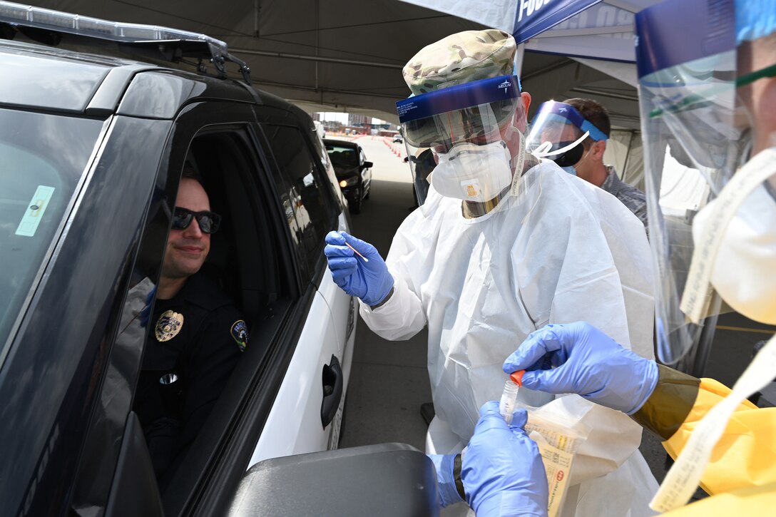 Photo of Lt. Col. Dwight Harley, of the 119th Medical Group taking a cheek swab from a Fargo police officer during a voluntary COVID-19 drive through testing process in the parking lot of the FargoDome, Fargo, N.D., April 25, 2020.