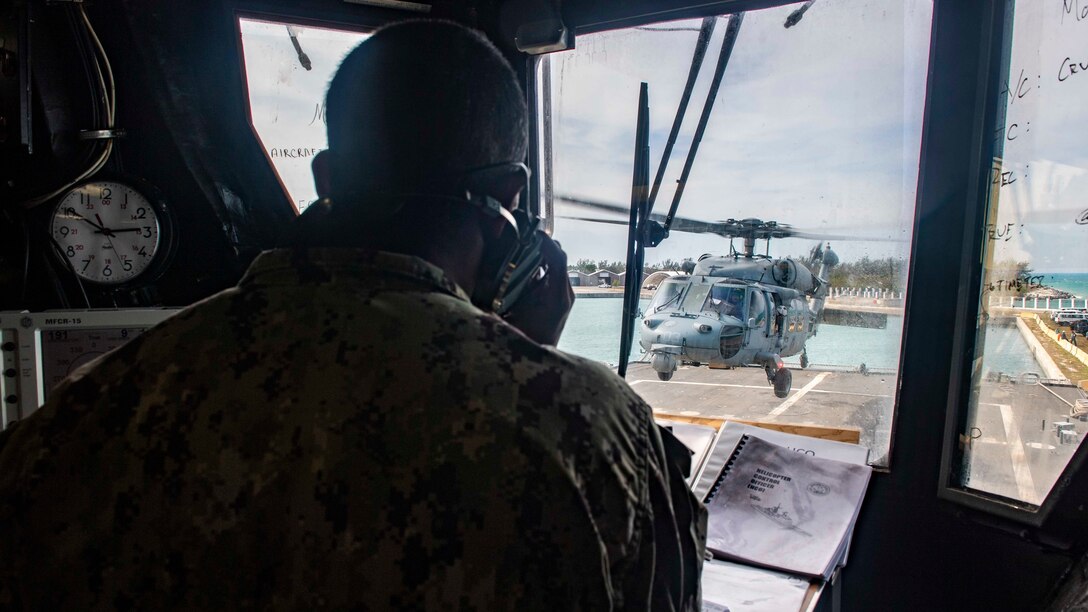 An air traffic controller on the phone while watching a helicopter take off.