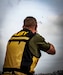 white male in green shirt and yellow and black vest wearing shoots a clay pigeon