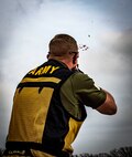 white male in green shirt and yellow and black vest wearing shoots a clay pigeon