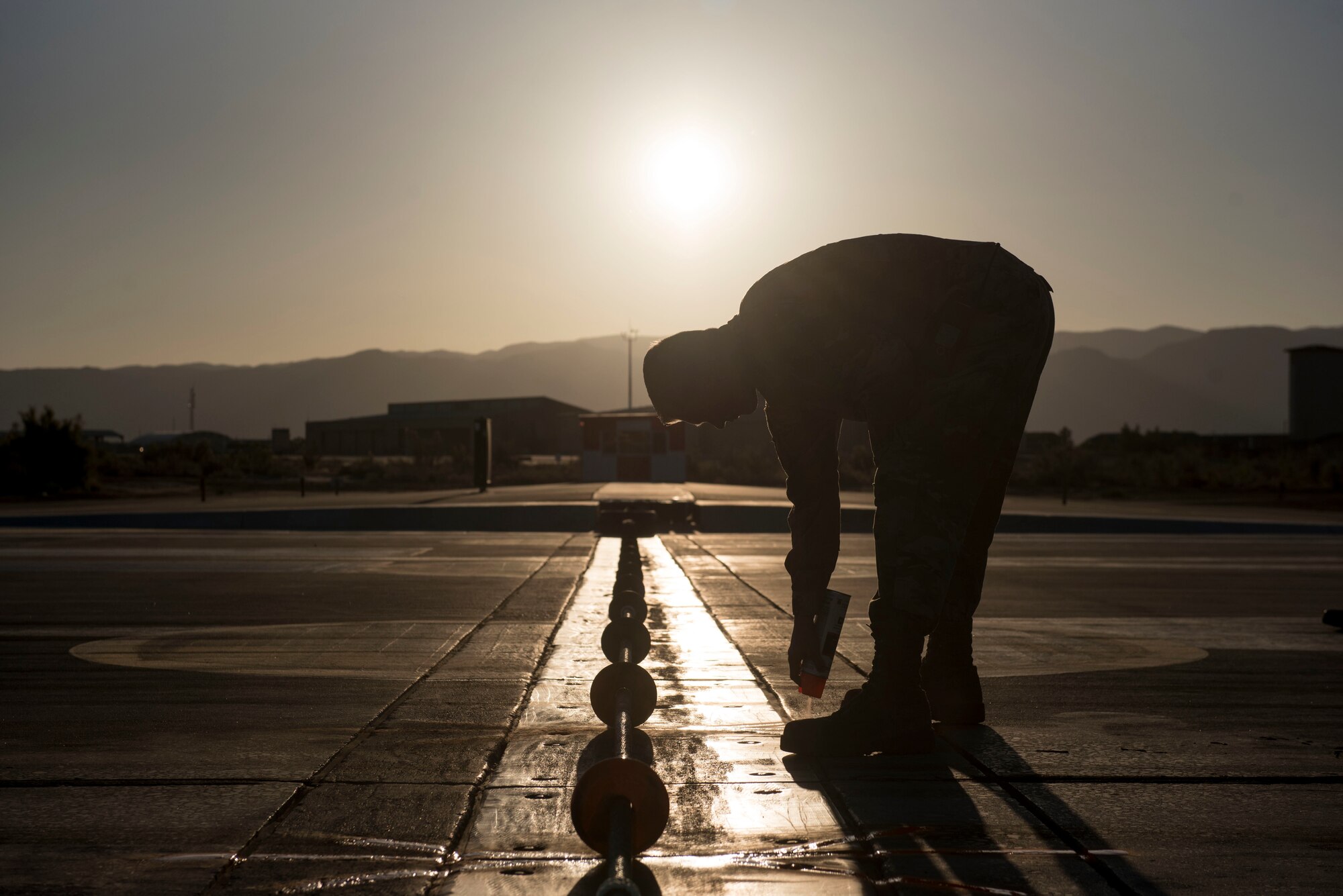 Senior Airman Wyatt Andrews, 49th Civil Engineer Squadron electrical power production technician, marks center support disks on the flightline, on Holloman Air Force Base, N.M., April 21, 2020. Andrews marks the disks to obtain proper spacing. The cable also sits 2 inches off the ground to engage an aircraft’s tailhook, in the event of an emergency. (U.S. Air Force photo by Staff Sgt. Christine Groening)