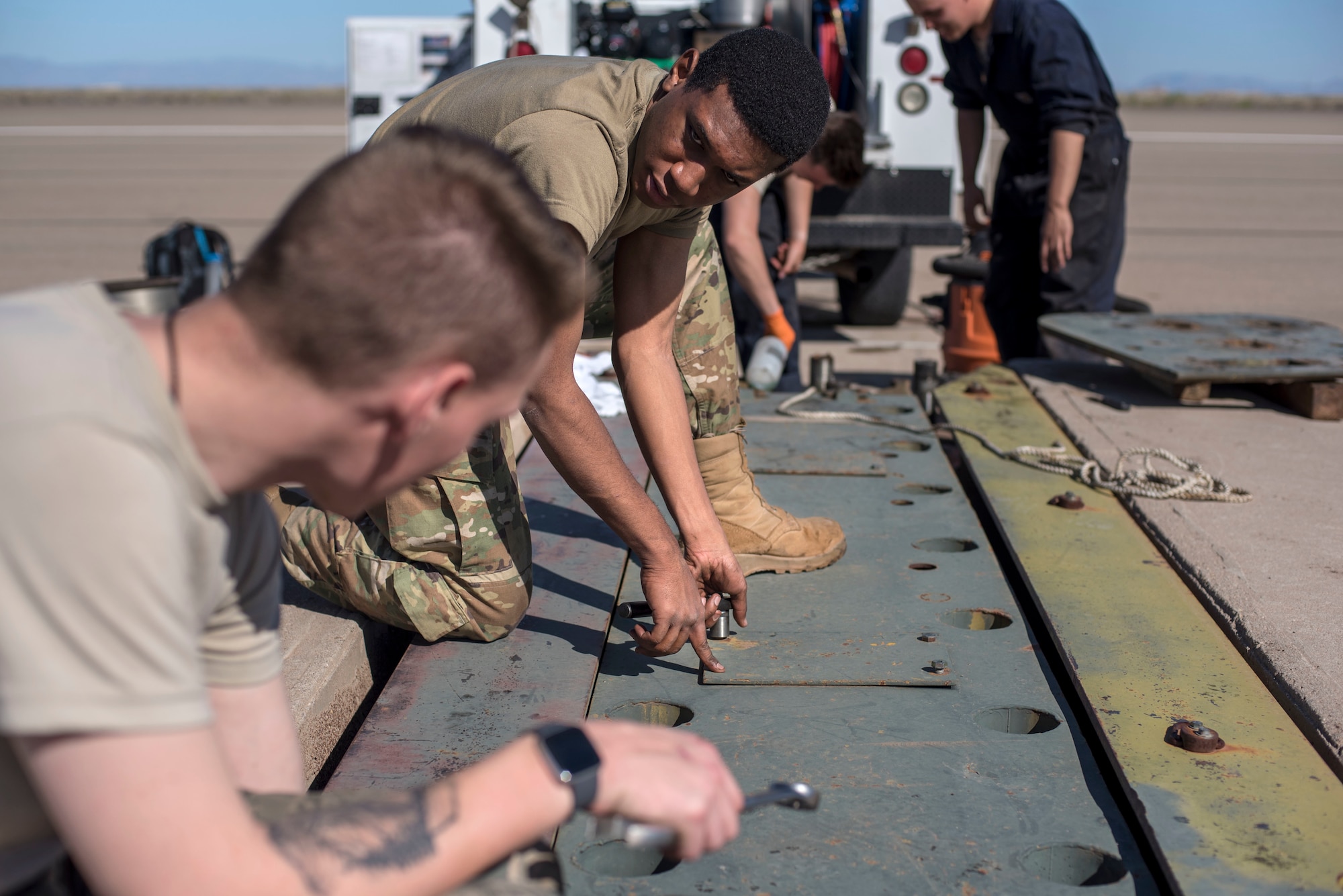 Airman 1st Class Sharn Lucas (center) and Airman 1st Class Nicholas Tirevold, 49th Civil engineer squadron electrical power production technicians, reinstall tape inspection plates on the flightline, on Holloman Air Force Base, N.M., April 21, 2020. The Airmen were conducting overhaul maintenance on the barrier system, which occurs every 42-months. (U.S. Air Force photo by Staff Sgt. Christine Groening)