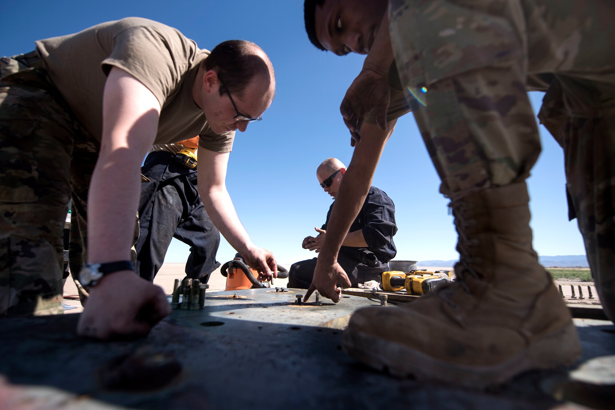 Airman 1st Class Curtis Mark (left) and Airman 1st Class Sharn Lucas (right), 49th Civil Engineer Squadron electrical power production technicians, reassemble a front sheave housing plate on the flightline, on Holloman Air Force Base, N.M., April 21, 2020. In addition to ensuring barriers are functional, they maintain power supply to buildings, as well as the anti-vehicle barriers found across the base. (U.S. Air Force photo by Staff Sgt. Christine Groening)