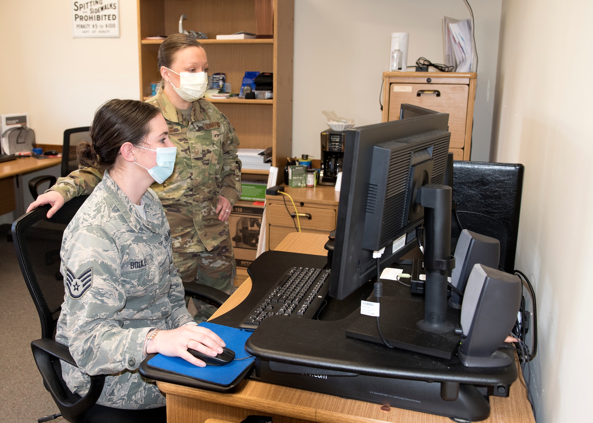 Two Airmen from Public Health stand in front a computer wearing face masks
