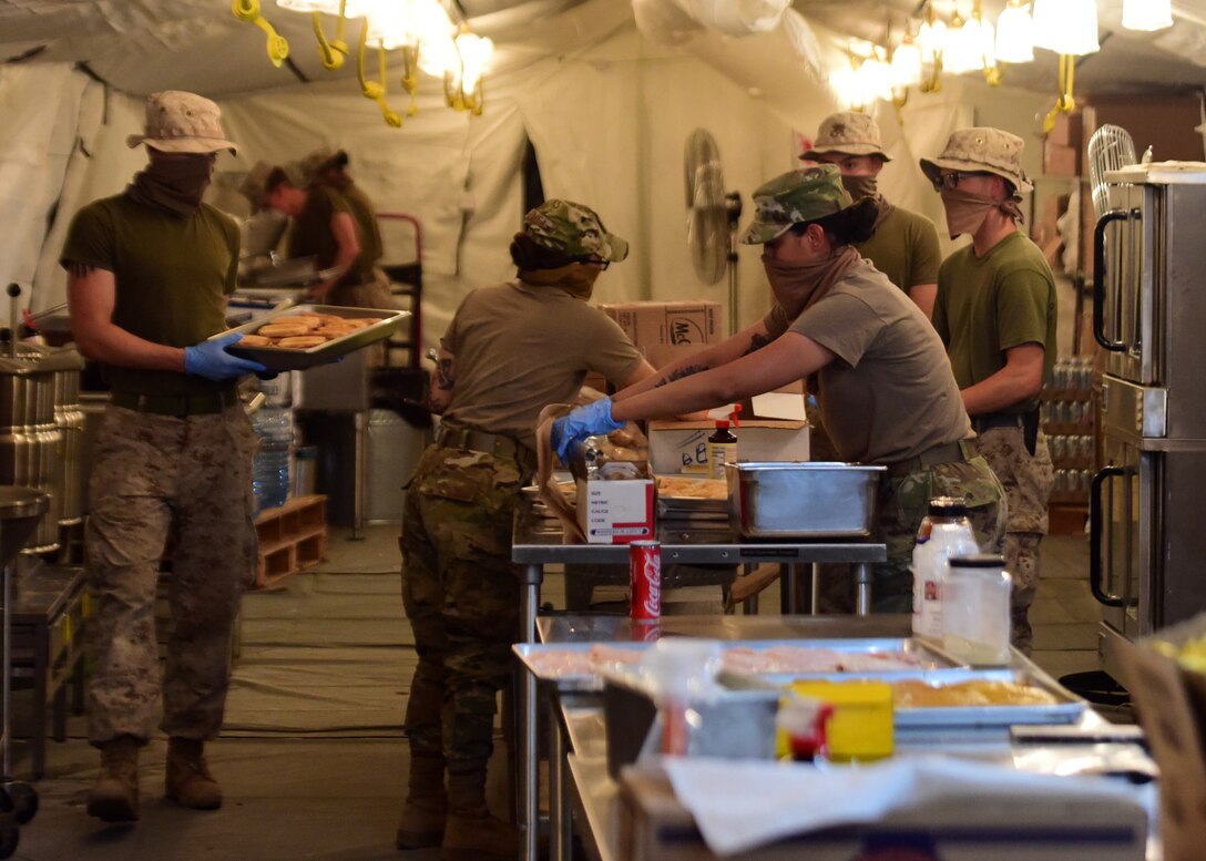 U.S. Airmen and Marine Corp volunteers prepare food at the Sandstorm field kitchen, Ahmed Al Jaber Air Base, Kuwait, April 17, 2020. The Sandstorm was stood up in an effort to further adhere to health protection levels by providing an additional avenue for customers to have a meal. (U.S. Air Force photo by Senior Airman Isaiah J. Soliz)