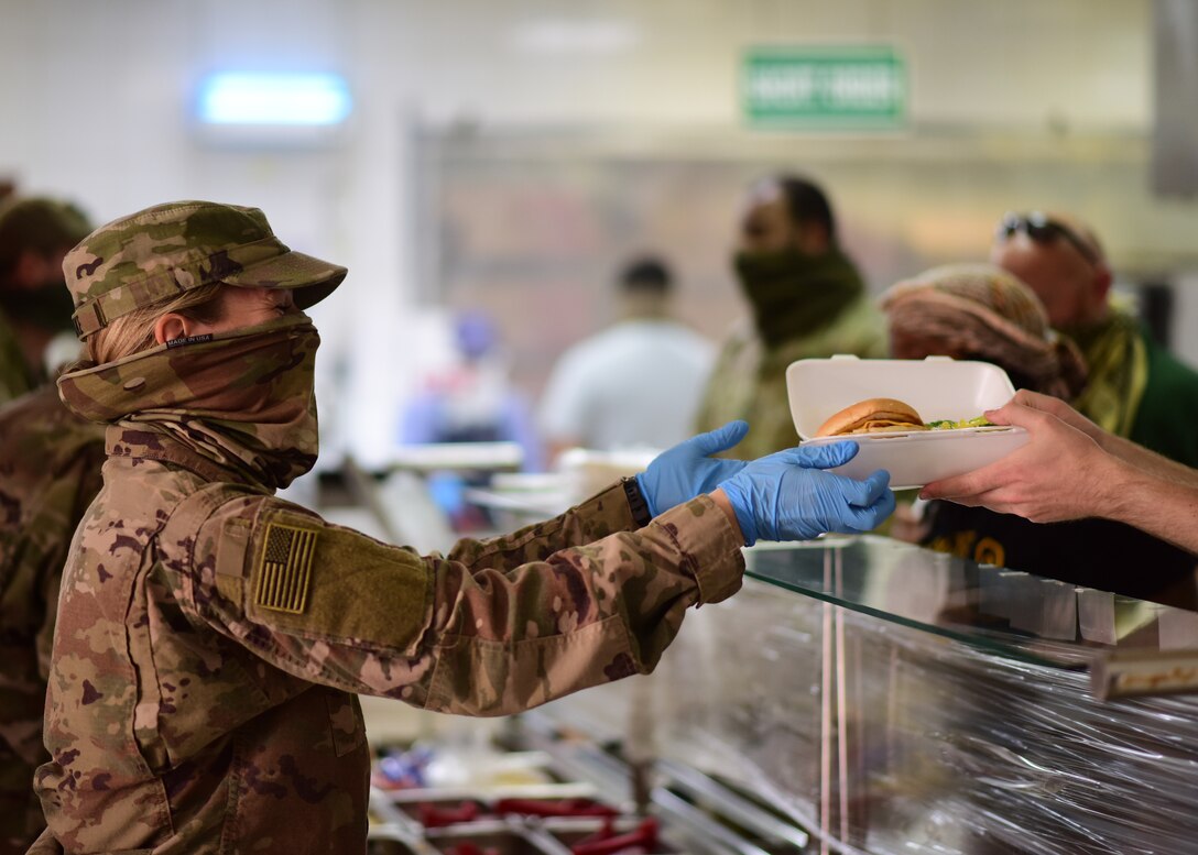 A volunteer from the U.S. Army Task Force Spartan hands a patron their meal at the Desert Winds Dining Facility, Ali Al Salem Air Base, Kuwait, April 16, 2020. Volunteers from across the installation have stepped up to help ensure the DFAC continues to remain open by promoting and enforcing heightened health protection guidelines. (U.S. Air Force photo by Senior Airman Isaiah J. Soliz)