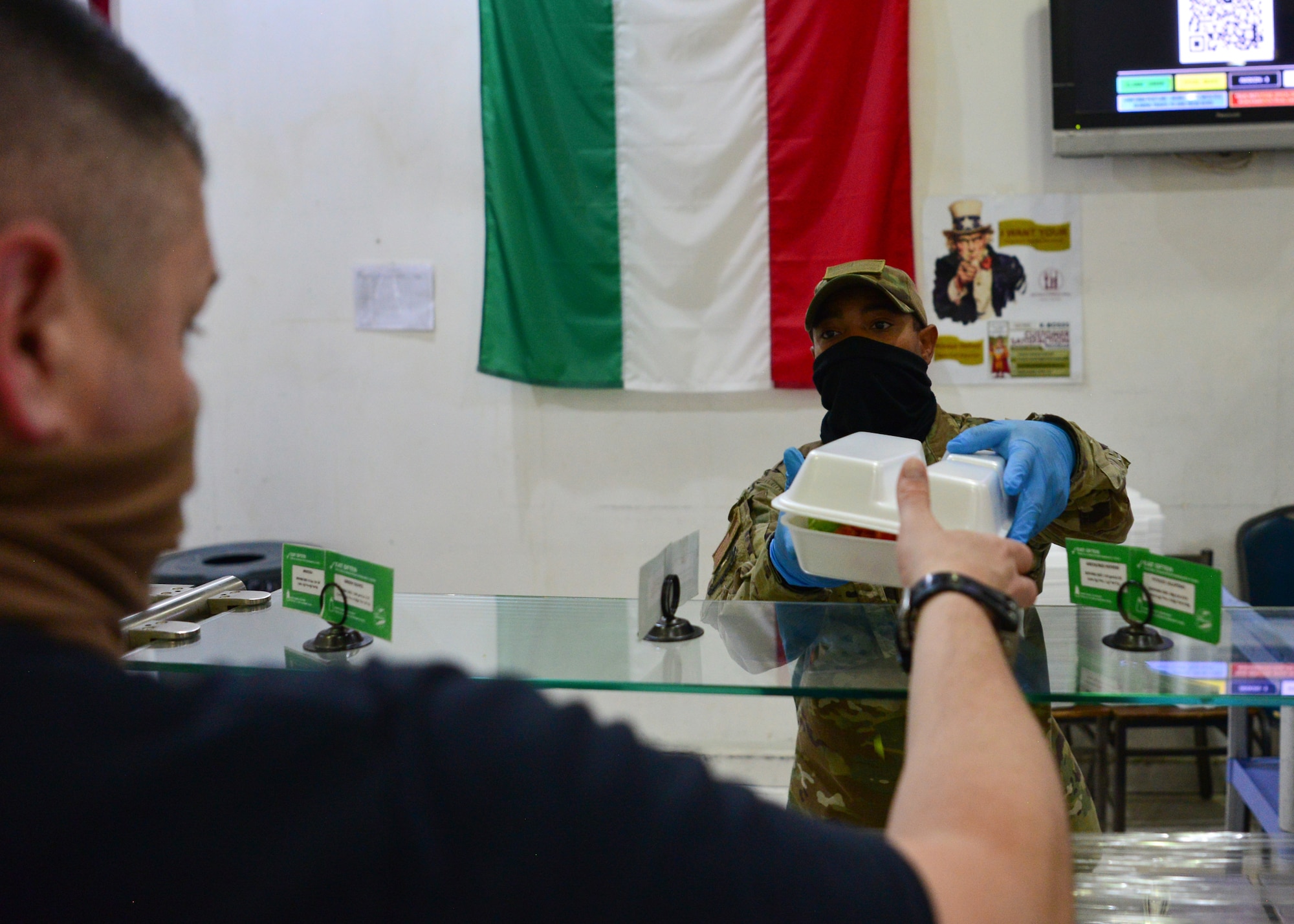 Tech. Sgt. Alexandre Montes, a volunteer, hands a customer their meal at the Desert Winds Dining Facility, Ali Al Salem Air Base, Kuwait, April 16, 2020. Volunteers from across the installation have stepped up to help ensure the DFAC continues to remain open by promoting and enforcing heightened health protection guidelines. (U.S. Air Force photo by Senior Airman Isaiah J. Soliz)