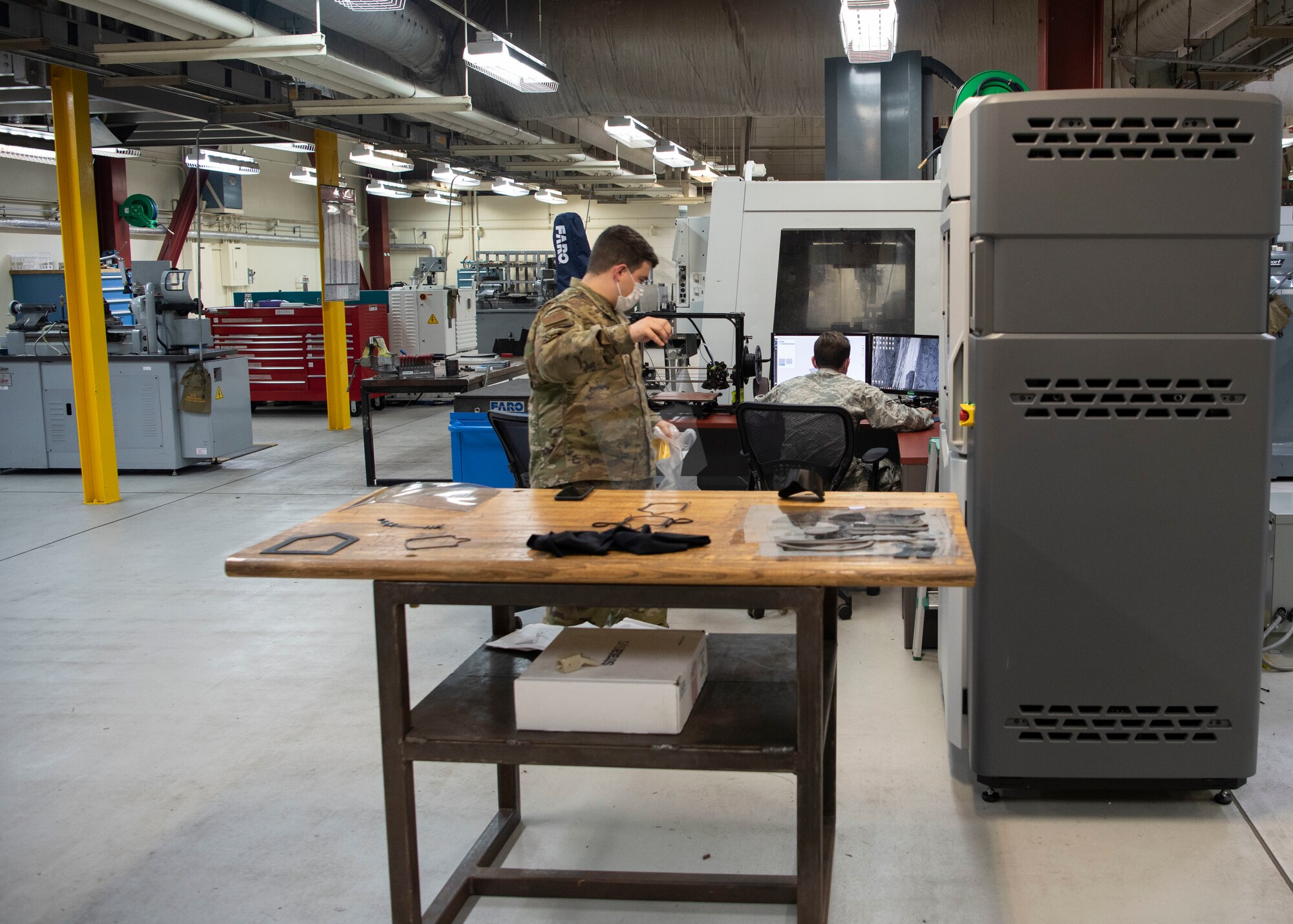 U.S. Air Force Staff Sgt. Adrian Gonzalez and Airman 1st Class Cyrus Bartony, from the 18th Equipment Maintenance Squadron, work together to 3D print a face shield April 9, 2020, at Kadena Air Base, Japan. Gonzalez and Bartony are the 3D print programmers that helped design the models to print personal protective equipment during COVID-19.