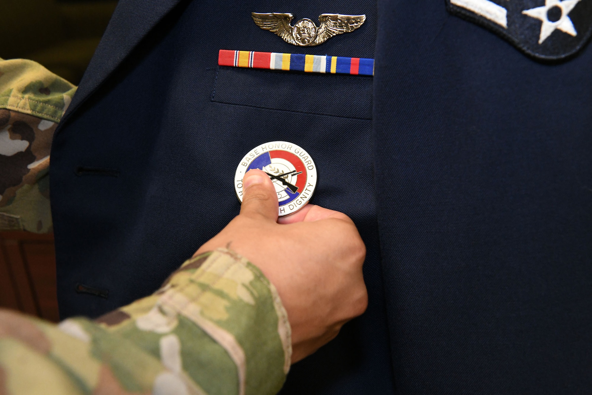 Photo is a closeup of a hand pinning the honor guard medallion to a uniform.
