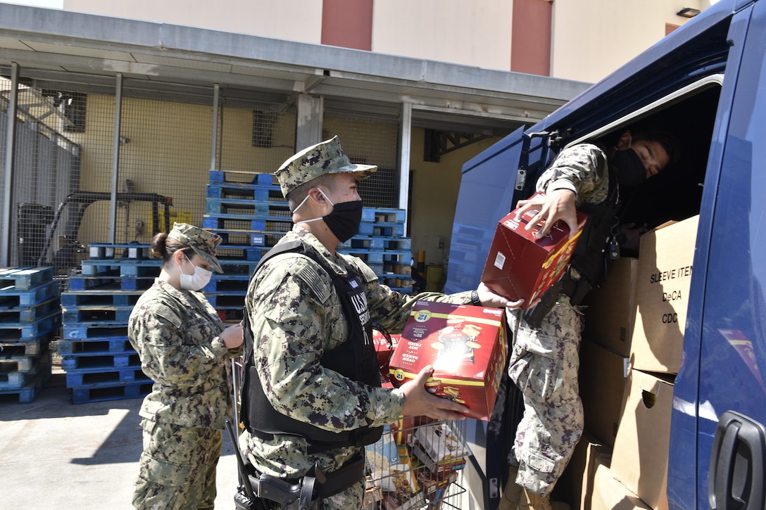 Sailors in uniform, all wearing face masks, load boxes into a van.