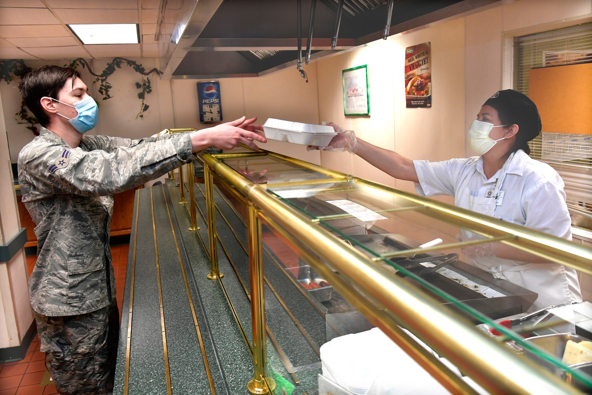 Airman 1st Class Logan Parent, 388th Aircraft Maintenance Squadron, is handed his lunch by Rosa Godinez, Hillcrest Dining Facility food services, at Hill Air Force Base, Utah, April 23, 2020. The food services contractor, Native Resource Development Company, Inc., is continuing to provide carry out meals for the base’s Airmen during the COVID-19 pandemic while keeping the dining facility extra clean and sanitized. (U.S. Air Force photo by Todd Cromar)