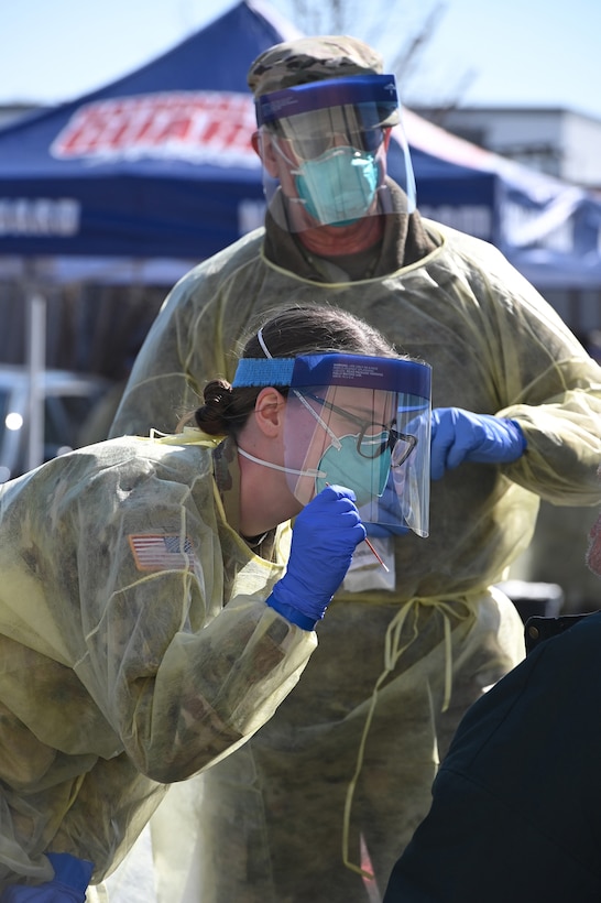 Photo of two North Dakota National Guard members wearing personal protective equipment as they administer COVID-19 test for a community member at a Fargo, N.D. testing site April 26, 2020.