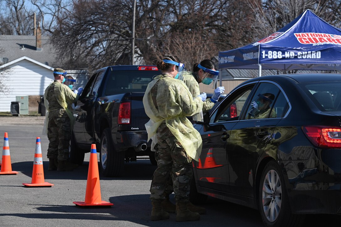 Photo of four North Dakota Air National Guard members wearing personal protective equipment as they conduct COVID-19 testing for community members in their automobiles at a testing site in Fargo, N.D., April 26, 2020.