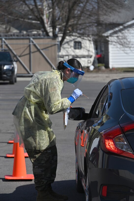 Photo of Senior Airman Kayla Dalquist leaning toward an automobile window to conduct a COVID-19 test for a community member at a testing site in Fargo, N.D., April 26, 2020.
