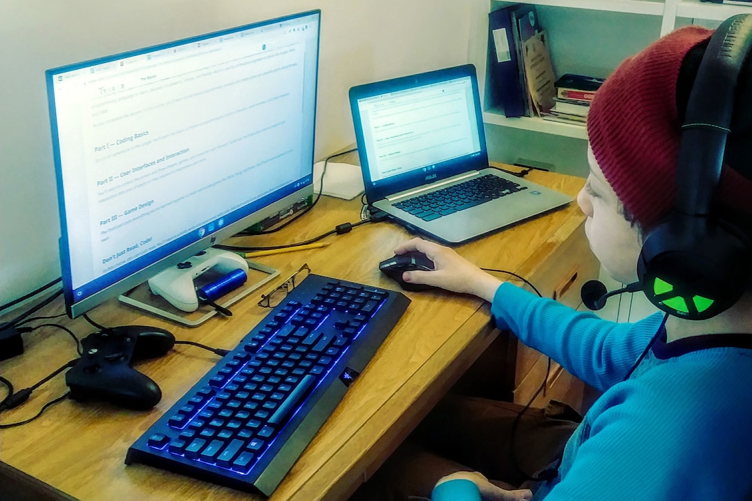 A boy in a stocking cap and wearing headphones looks at a computer screen.