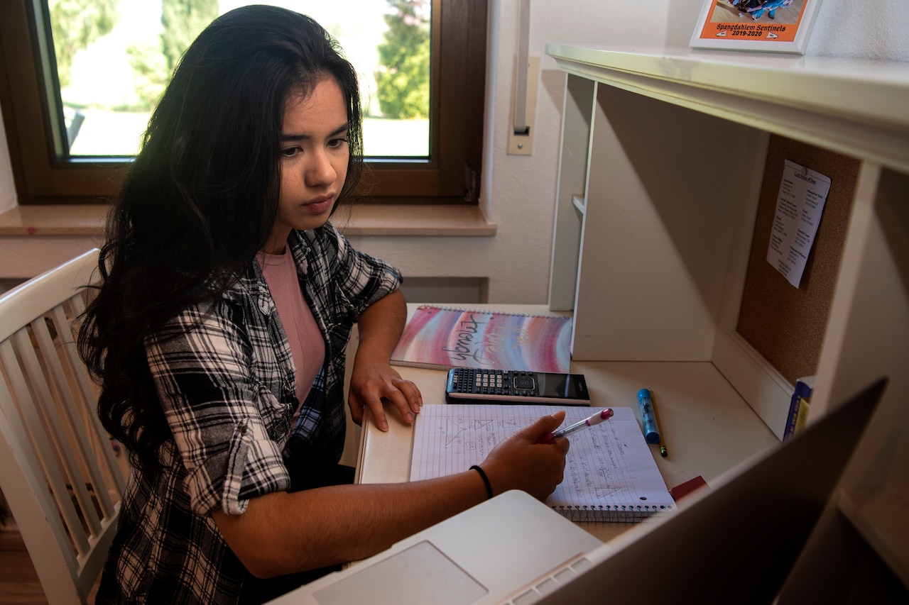 A young lady holds pen to paper as she looks at a computer screen.