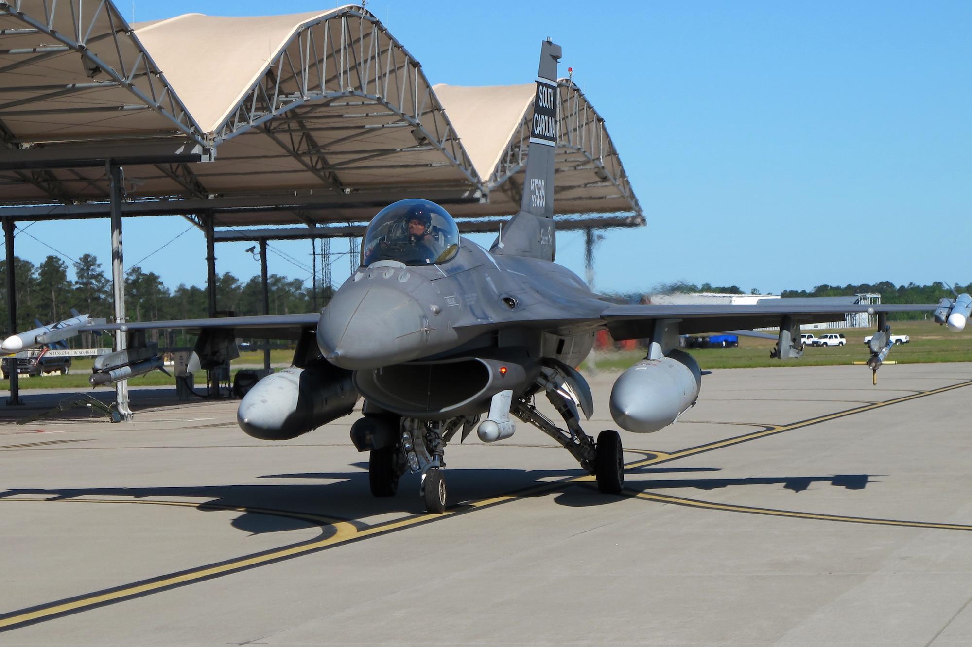 An F-16 fighter jet taxis under a blue sky toward the runway for takeoff.