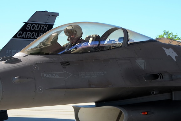 An F-16 pilot prepares for takeoff at under a bright blue sky and bright sun.