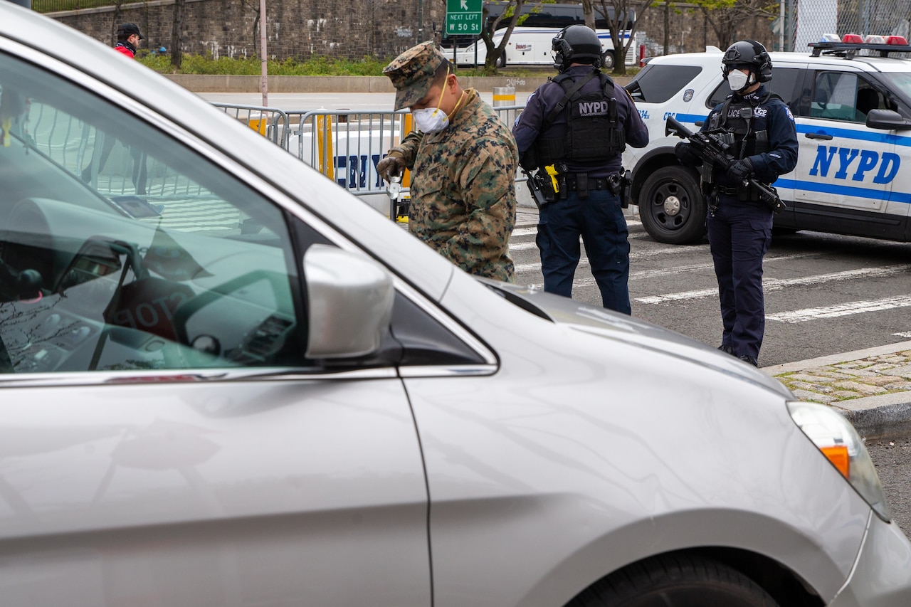 A New York City police officer and a Marine screen a vehicle.