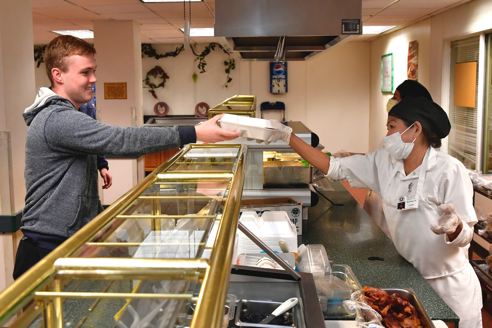 Airman 1st Class Dalton Tilt, 388th Aircraft Maintenance Squadron, is handed his lunch by Rosa Godinez, Hillcrest Dining Facility food services, at Hill Air Force Base, Utah, April 23, 2020. The food services contractor, Native Resource Development Company, Inc., is continuing to provide carry out meals for the base’s Airmen during the COVID-19 pandemic while keeping the dining facility extra clean and sanitized. (U.S. Air Force photo by Todd Cromar)