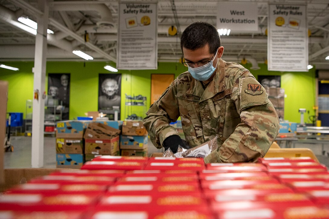 An airman wearing gloves and a face maks sorts red food containers on a table.