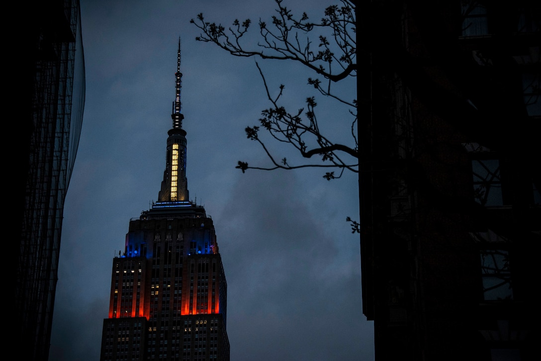 Orange, white and blue lights illuminate the top of the Empire State Building.