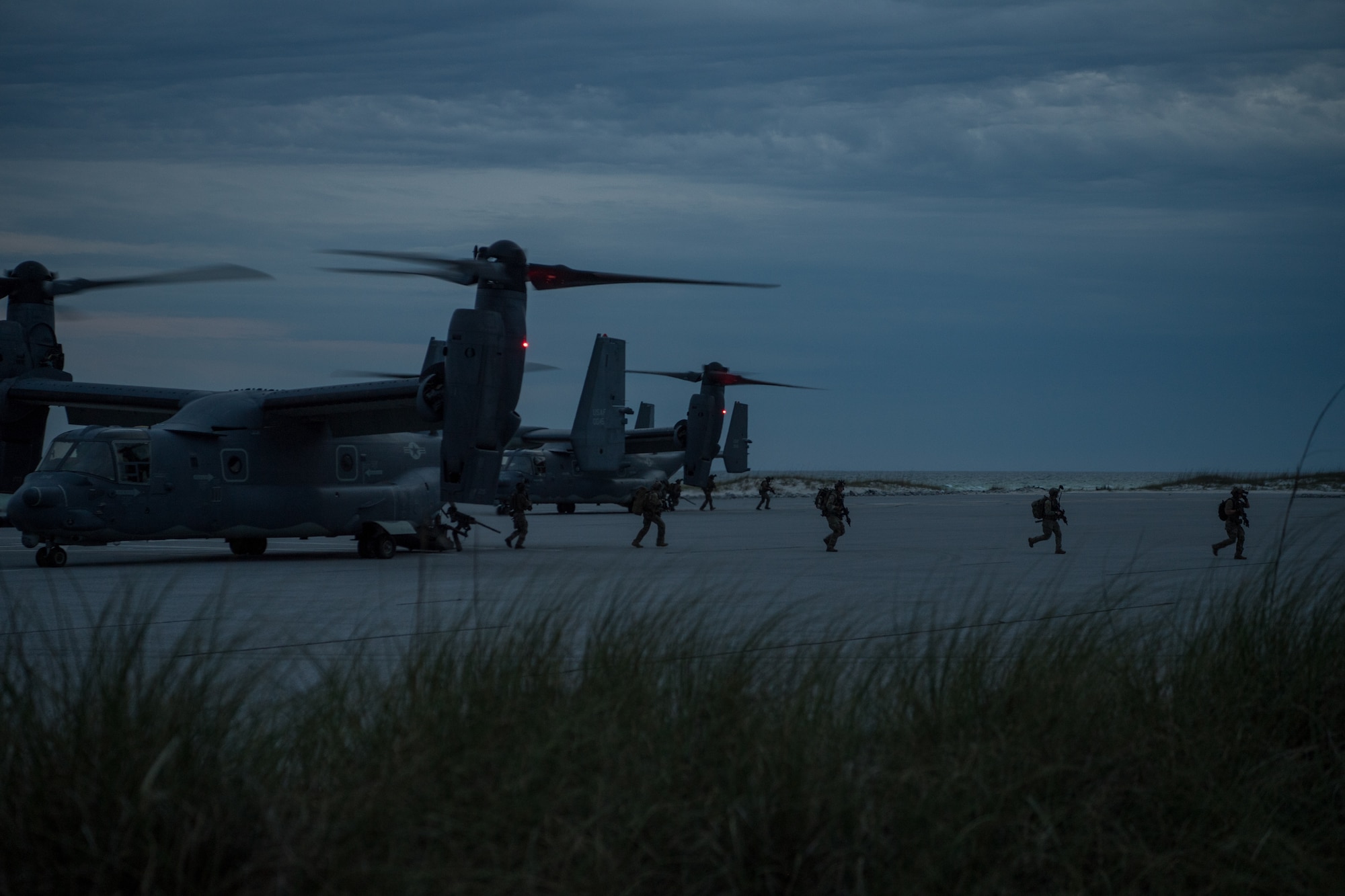 rotary aircraft sit on a landing zone with airmen walking out onto a beach