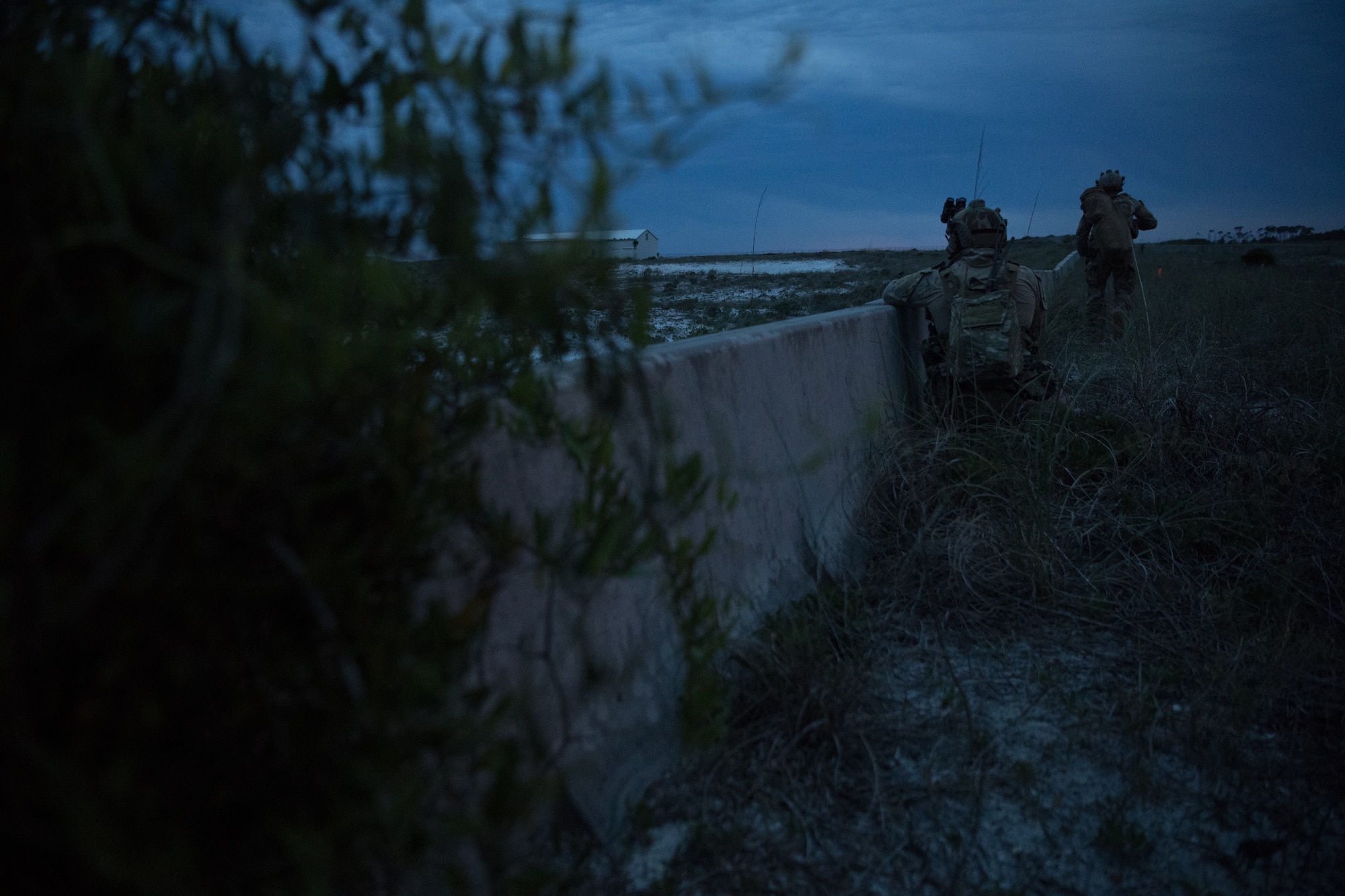 two airmen stand behind a wall looking over a mountain side