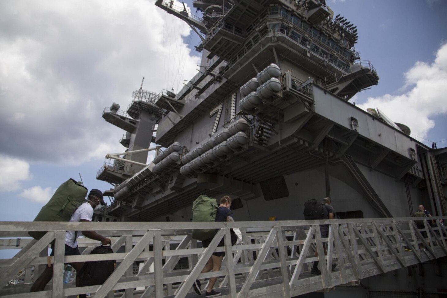 Sailors assigned to the aircraft carrier USS Theodore Roosevelt (CVN 71) embark the ship after weeks of cleaning and essential watch standing. Thousands of Sailors from Theodore Roosevelt were moved to local hotels in an effort to implement an aggressive mitigation strategy to minimize the spread of COVID-19 and protect the health of the Sailors. Theodore Roosevelt's essential watch standers and cleaning team conducted a crew swap April 29, turning over a clean ship to a COVID negative crew after completion of their off-ship quarantine or isolation.