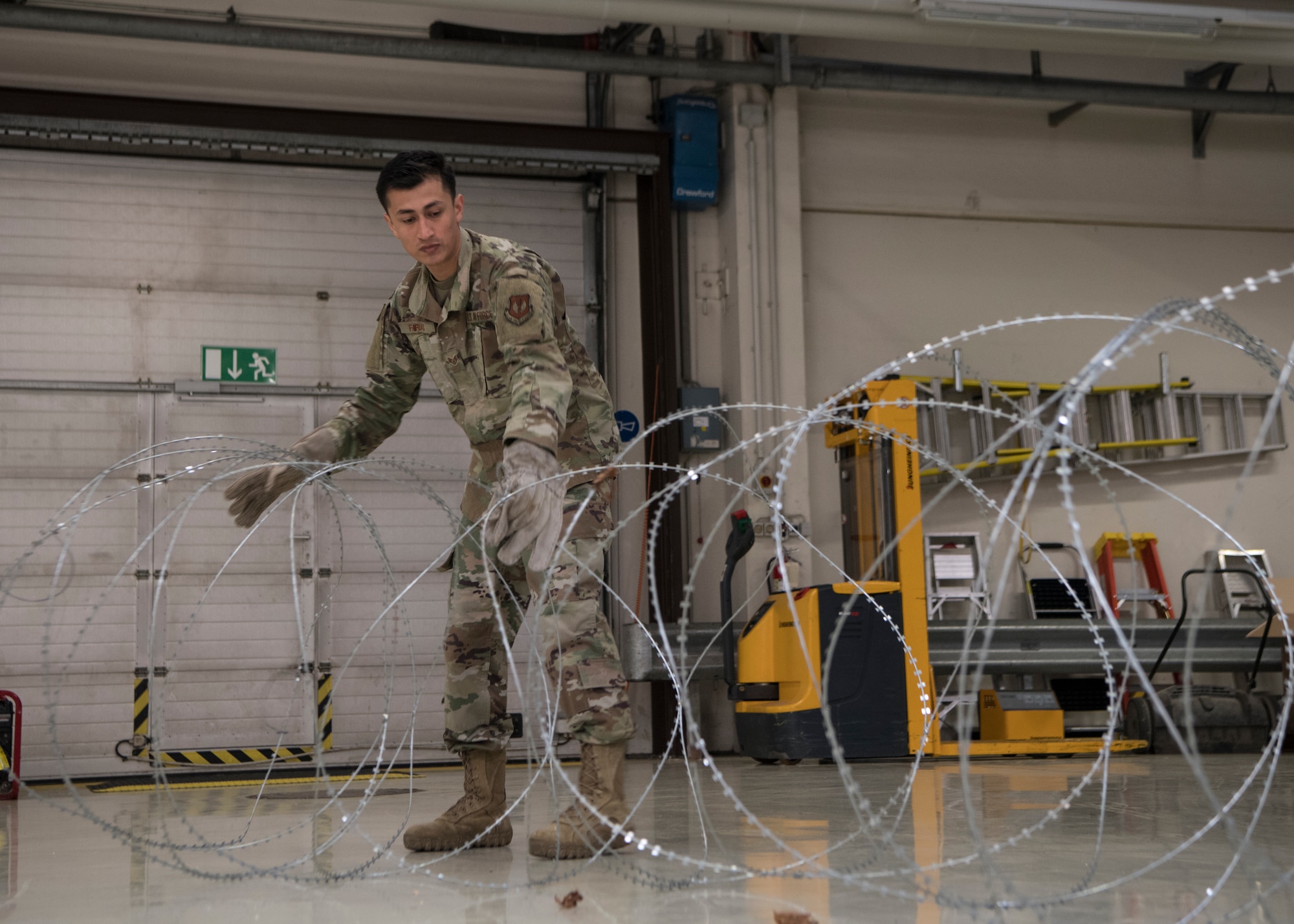 U.S. Air Force Staff Sgt. Abraham Farias, 786th Civil Engineer Squadron expeditionary engineering training manager, uncurls a roll of barbed tape at Ramstein Air Base, Germany, April 23, 2020