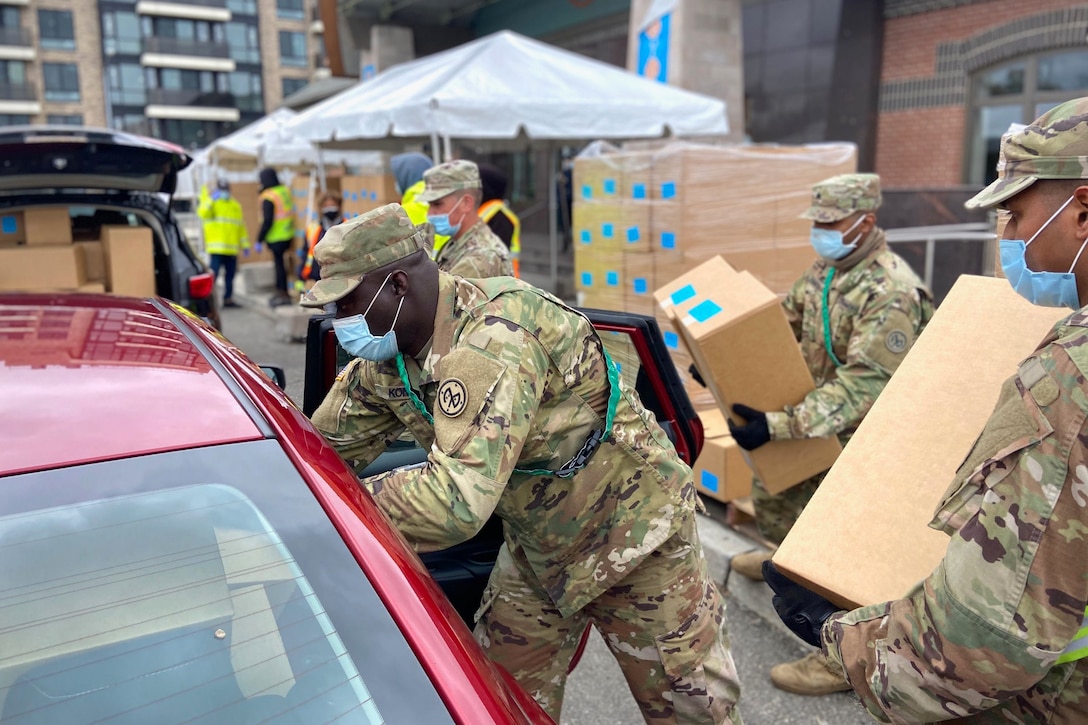 Service members wearing face masks give boxes to people in cars.