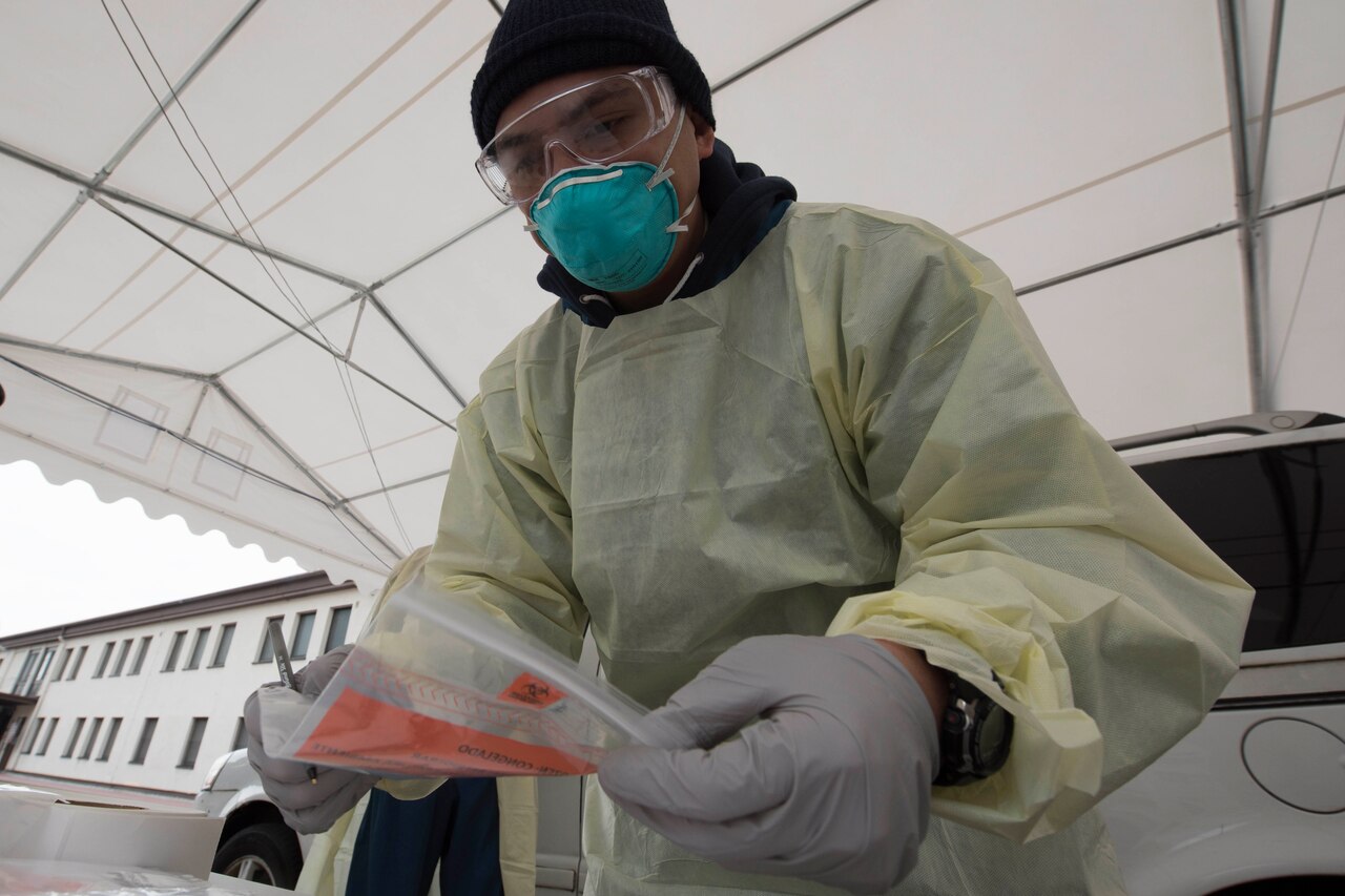 A man wearing personal protective equipment holds a sealed plastic bag.