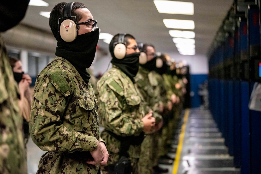 Navy recruits wearing face mask stand in a line.