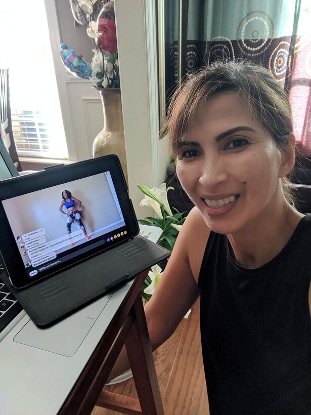 Photos shows a woman sitting in front of her tablet with fitness instructor giving a class on the screen.