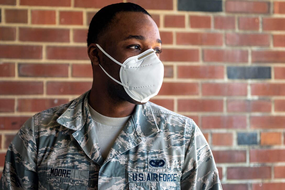 An airman wearing a mask stands in front of a building.