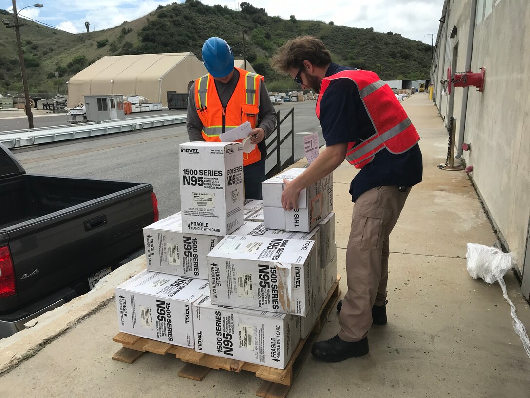 Two men with orange safety vests pick up white boxes