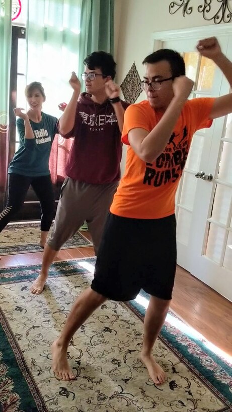 Photo shows a family, father, son and wife, doing Zumba in their house.