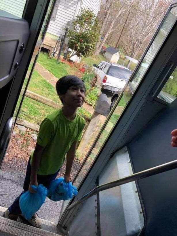 A boy on a school bus smiles after receiving bags of lunch.